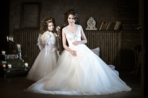 a bride wearing a beautiful wedding dress standing beside her sister who is wearing a white dress.