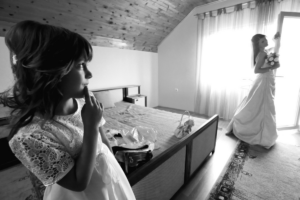 a black and white image of a girl in a wedding dress and her sister looking at her from across the room